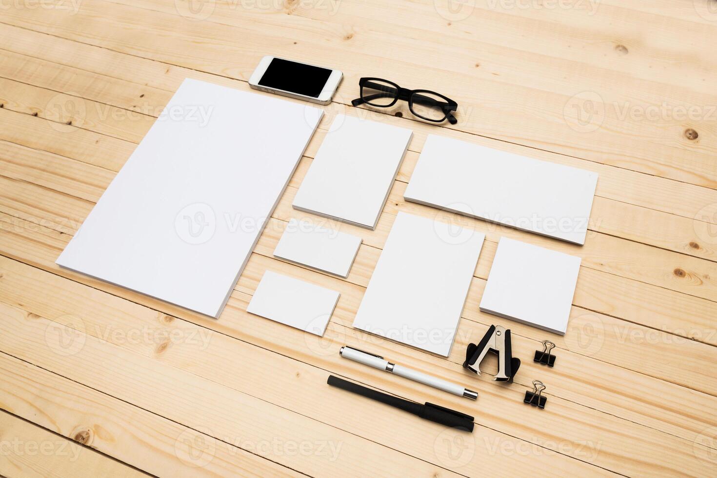 Workspace arrangement with blank stationery, smartphone, and reading glasses on wooden surface photo