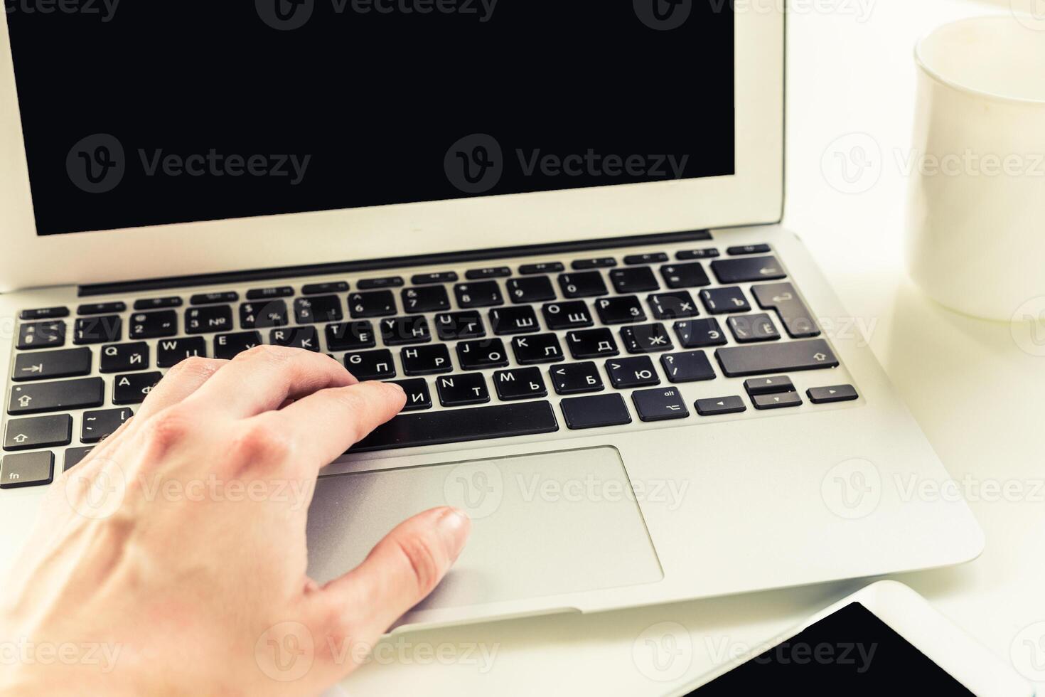 Hand typing on a laptop keyboard while sitting at a desk with a cup nearby in a bright workspace photo