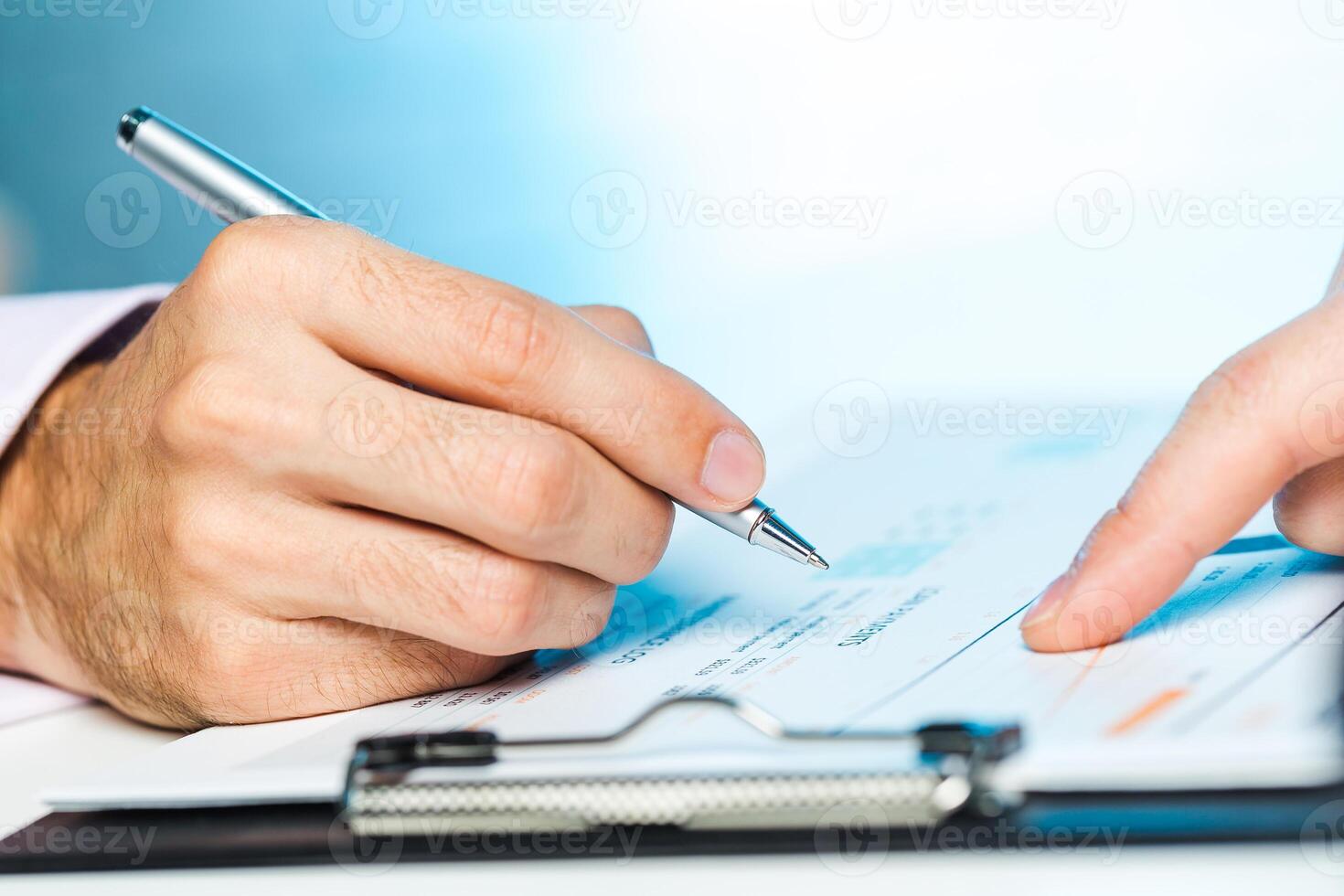 Person signing a document at a desk in a well-lit office setting during the afternoon photo