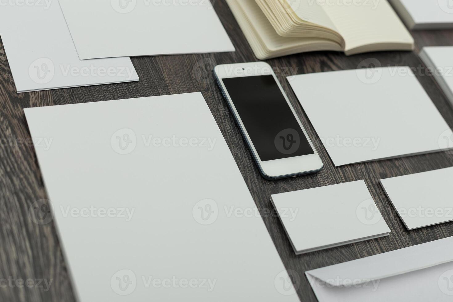 Blank sheets, notebook, and a smartphone arranged on a wooden table for creative work or planning sessions photo