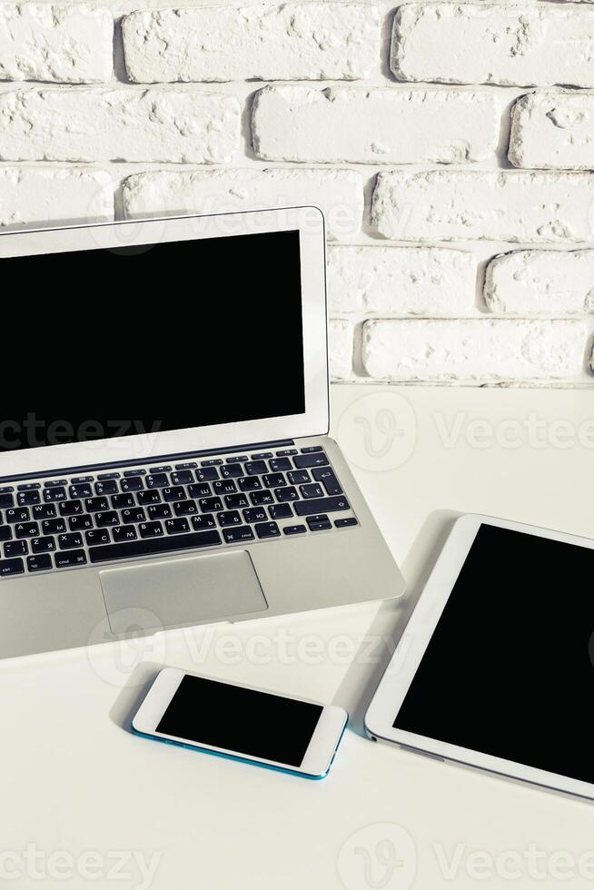 Workspace setup with laptop, tablet, and smartphone on a white brick background for productivity and creativity photo