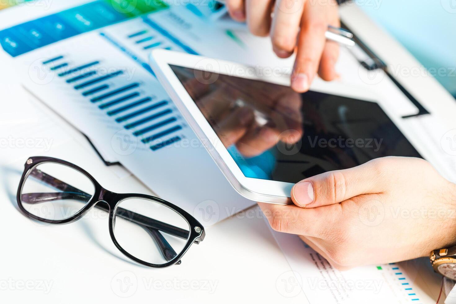 Professional analyzing data on tablet while reviewing charts and graphs in modern workspace photo