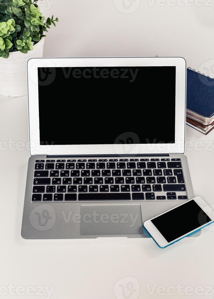 Workspace with a laptop and smartphone placed on a table beside a plant and notebook in a bright setting photo