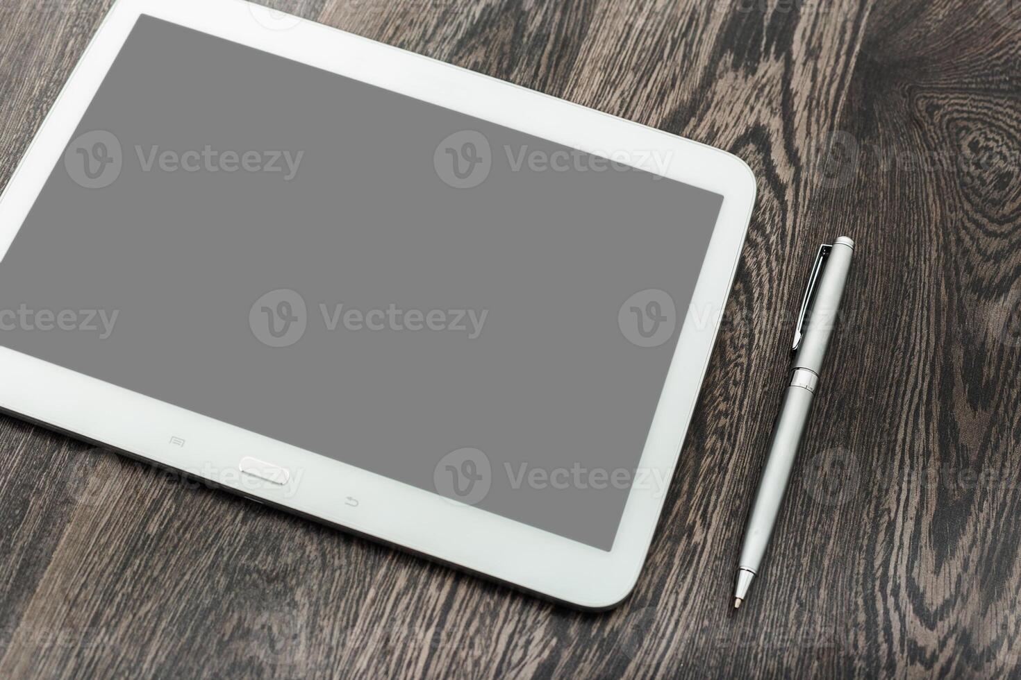 Stylish tablet and pen resting on dark wooden surface, ideal for creative work or note-taking in a modern workspace photo