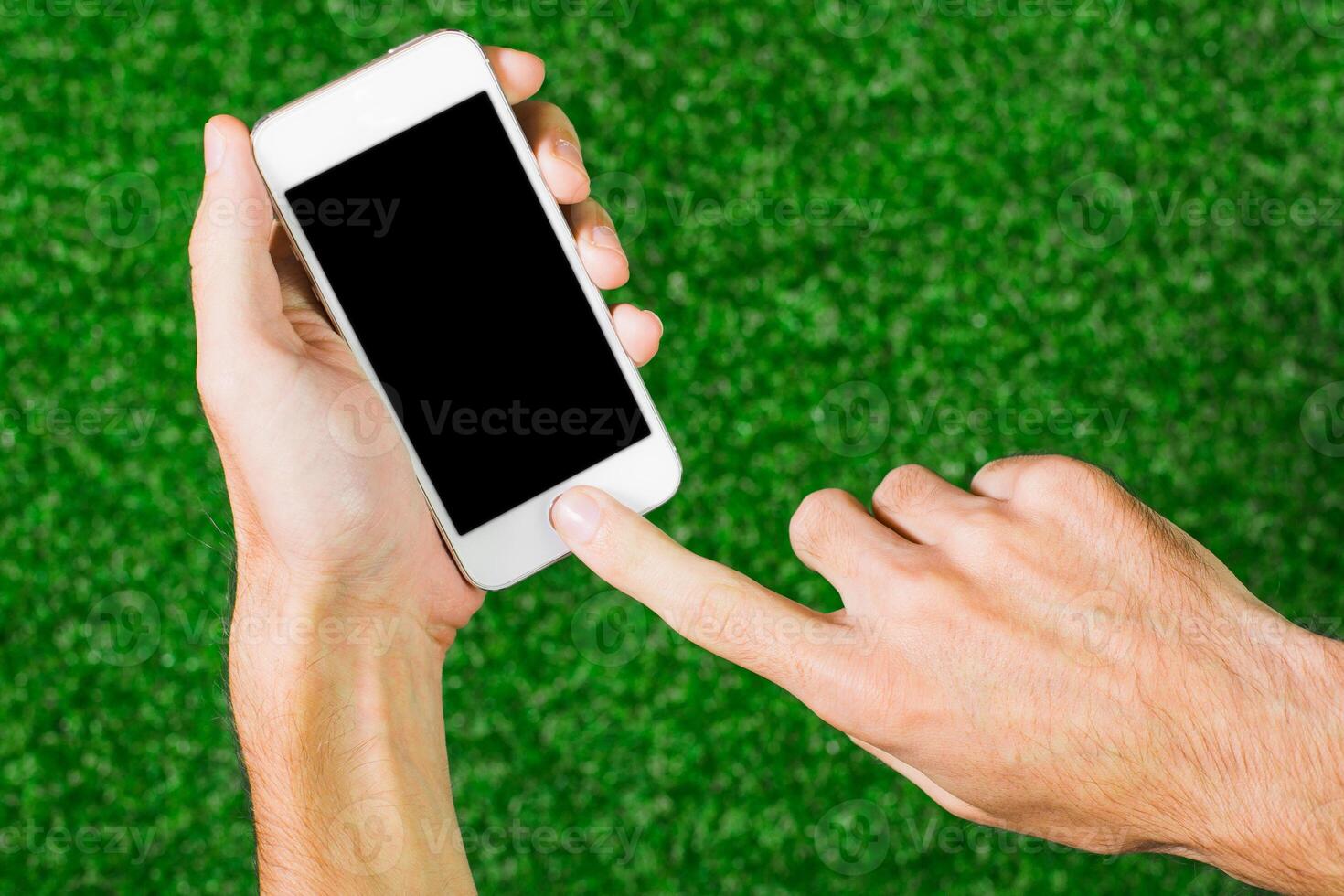 Person using smartphone on green grass surface during sunny day while engaging with digital content or application photo