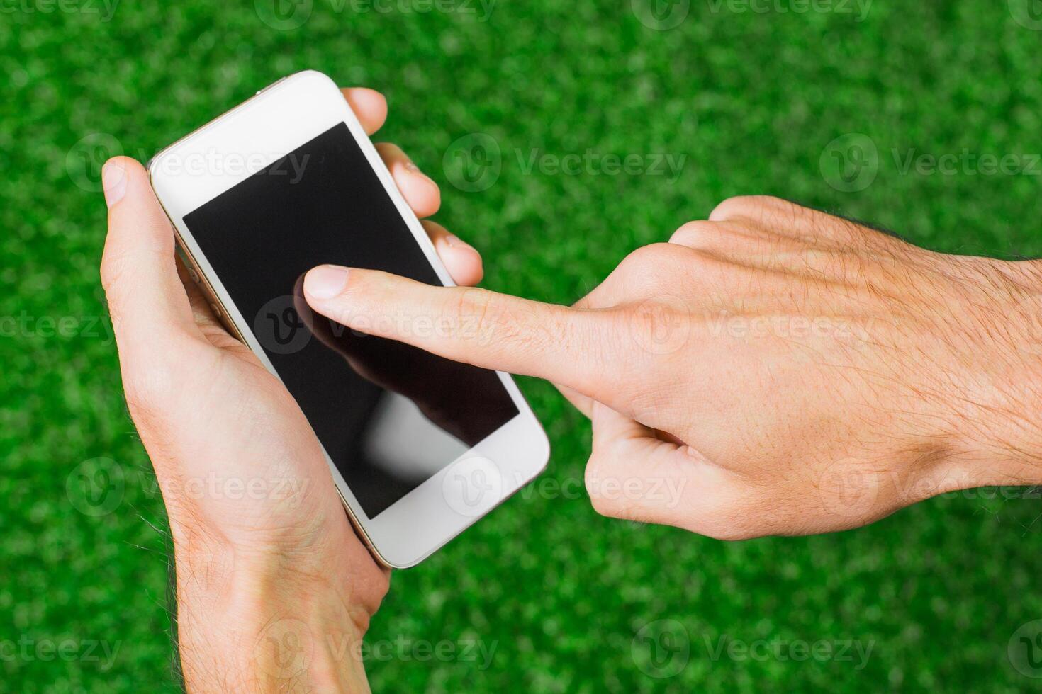 Person using a smartphone on green grass surface while interacting with an application in bright daylight photo