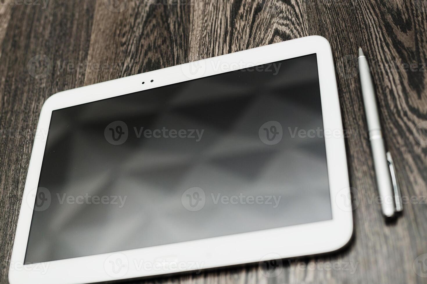 Digital tablet placed on a wooden surface next to a silver pen during a bright, productive work session photo