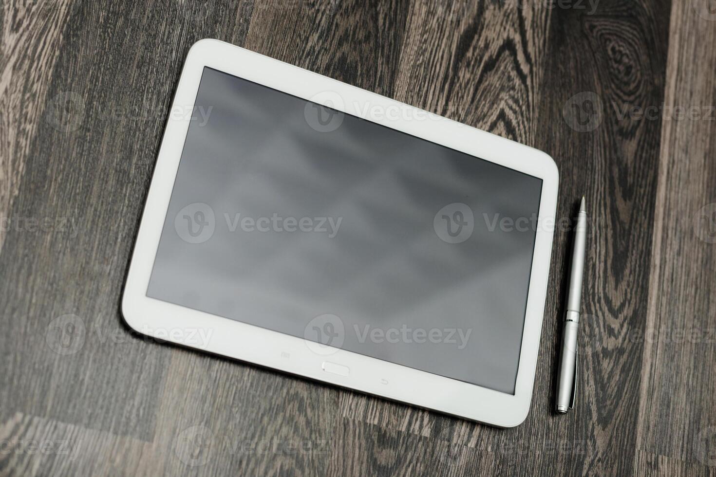 Tablet and pen resting on wooden surface in a modern workspace during daylight hours photo