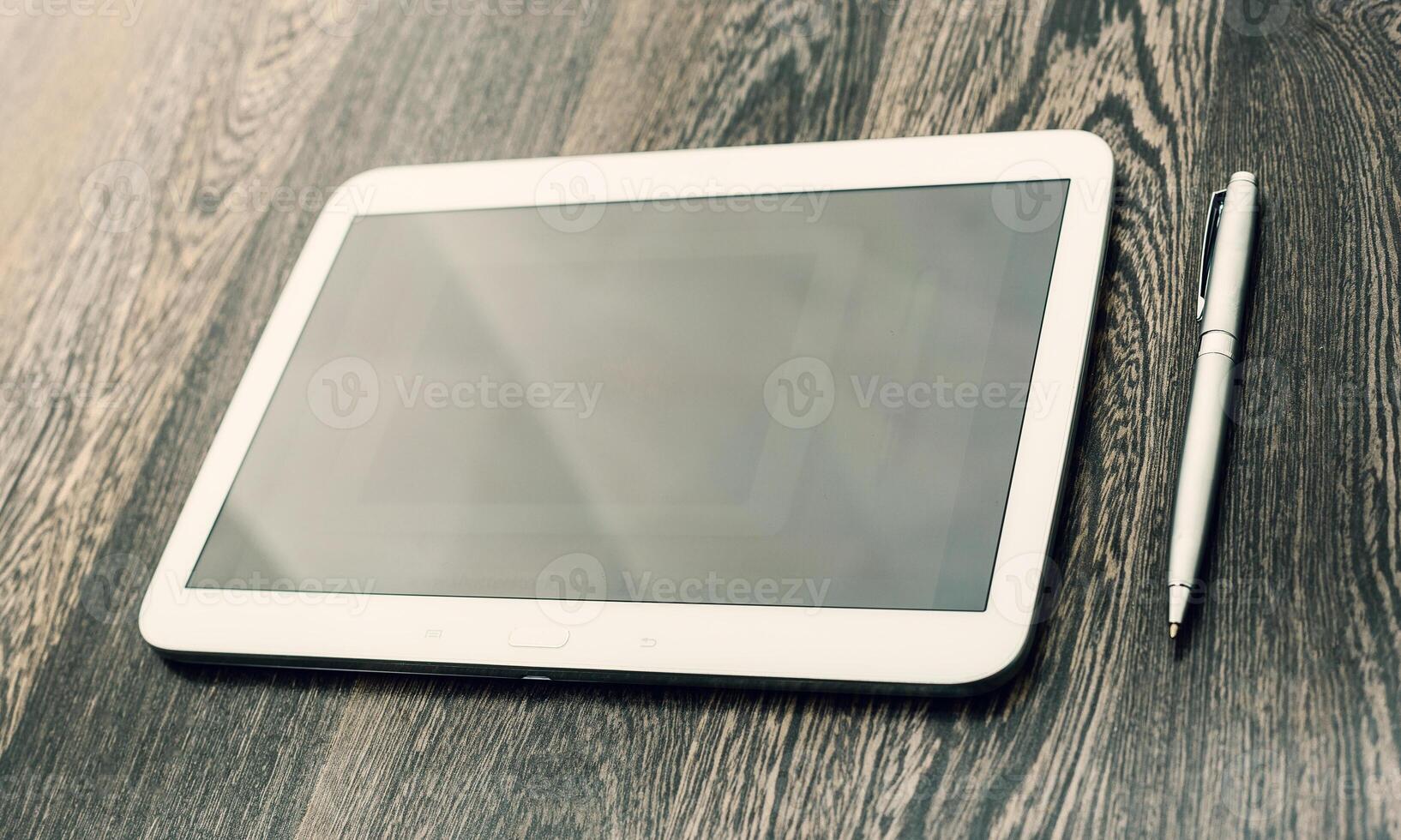 Digital tablet placed on wooden table with a pen nearby, showcasing workspace essentials for productivity photo