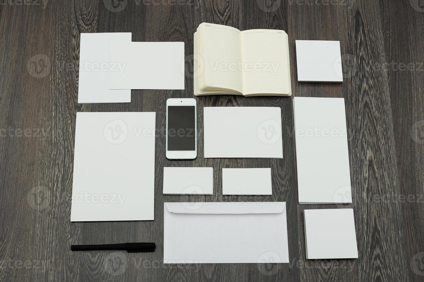 Workspace arrangement featuring blank stationery, smartphone, and notebook on wooden table photo
