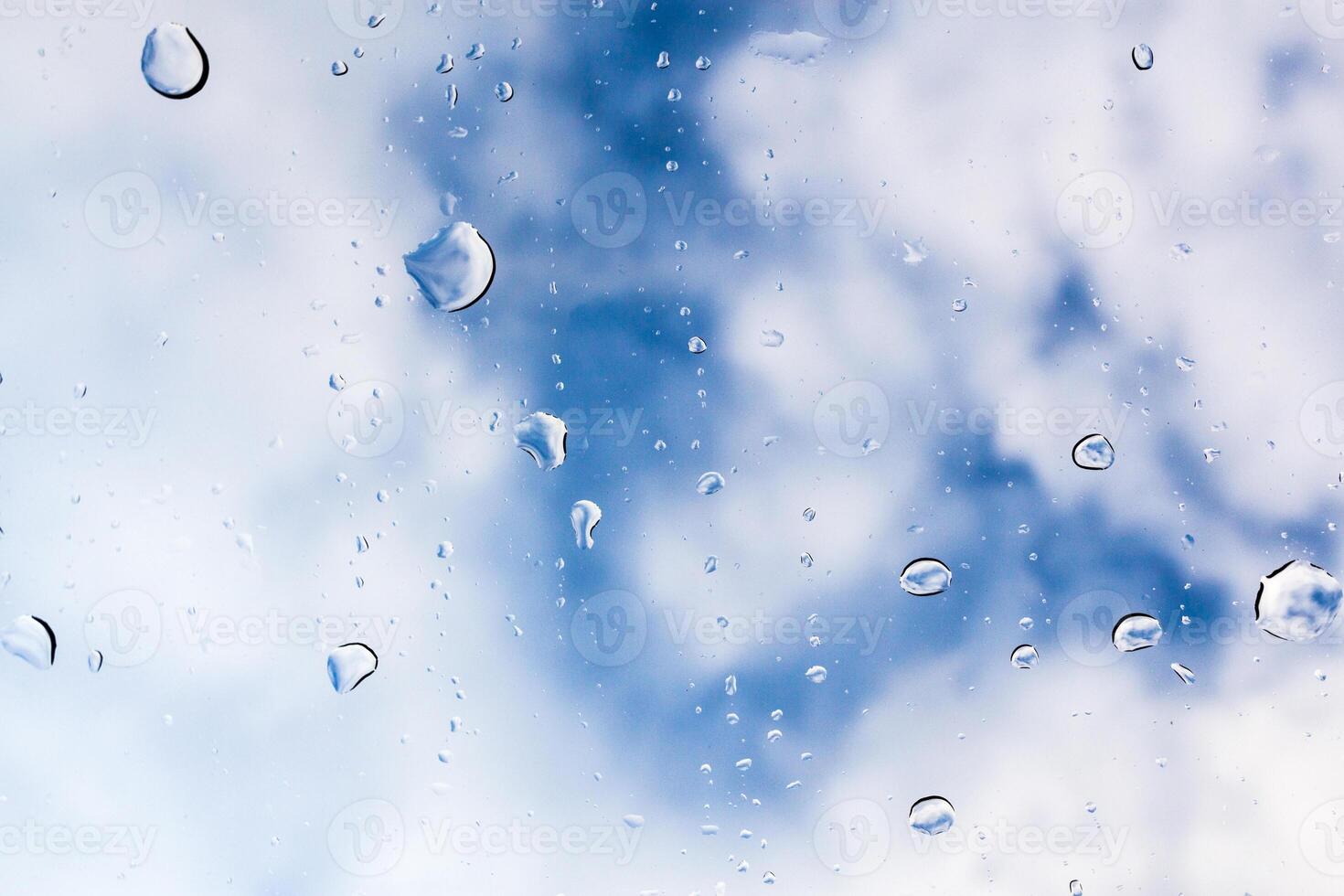 Raindrops cling to a window with a backdrop of blue sky and clouds in a serene afternoon photo