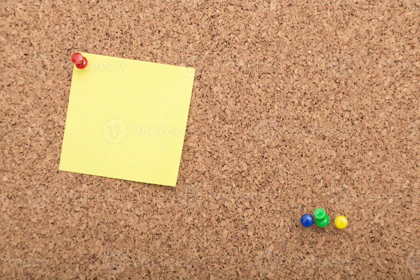 Colorful push pins and a yellow sticky note on a cork bulletin board in a home office setting photo