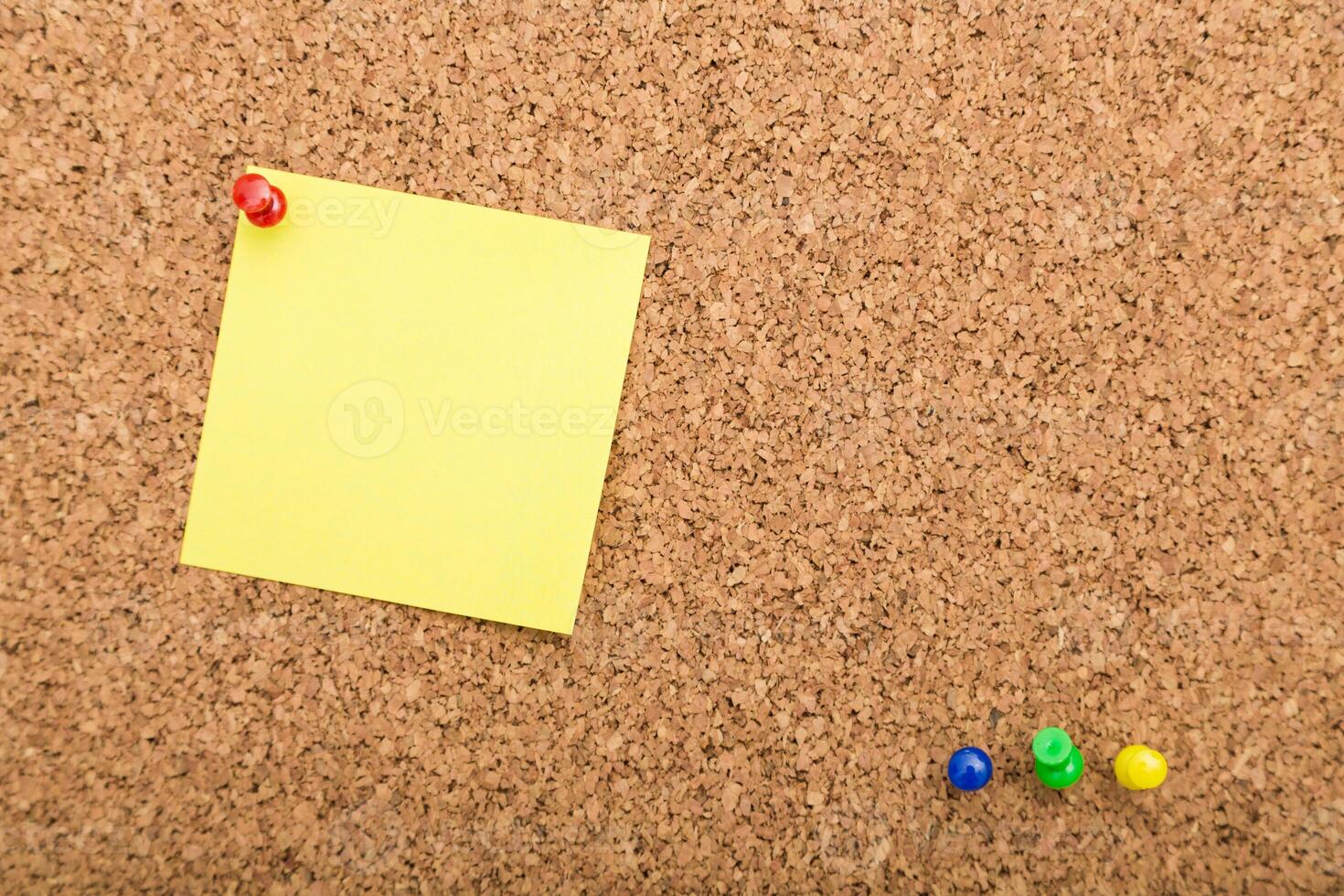 Yellow sticky note on corkboard with colored push pins arranged for task reminders or planning photo