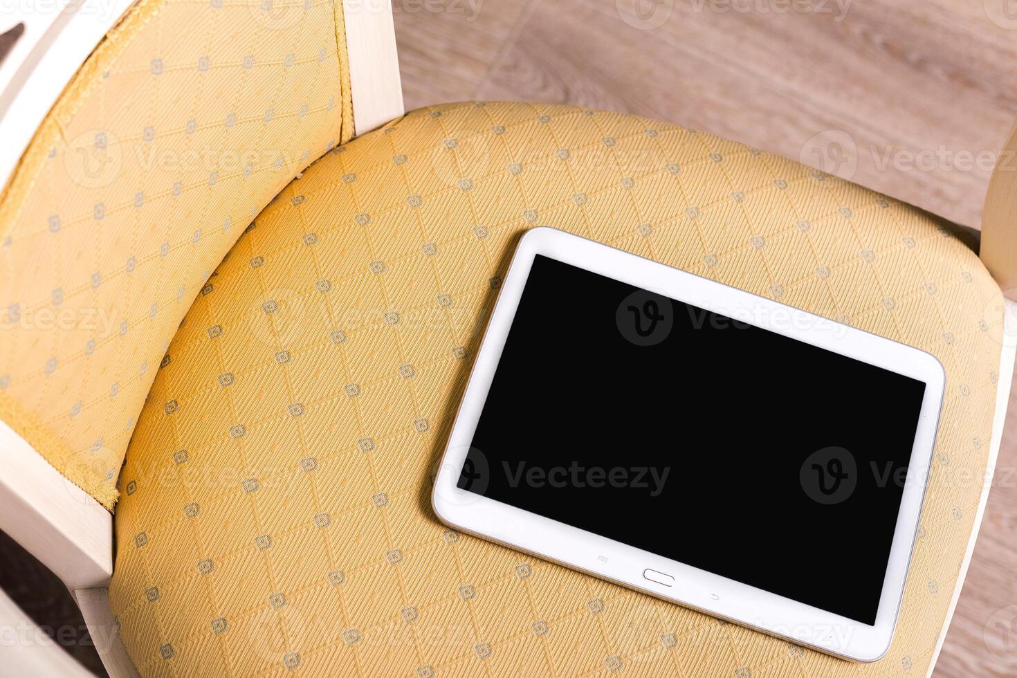 Tablet rests on patterned chair cushion in a cozy indoor setting during daylight hours photo