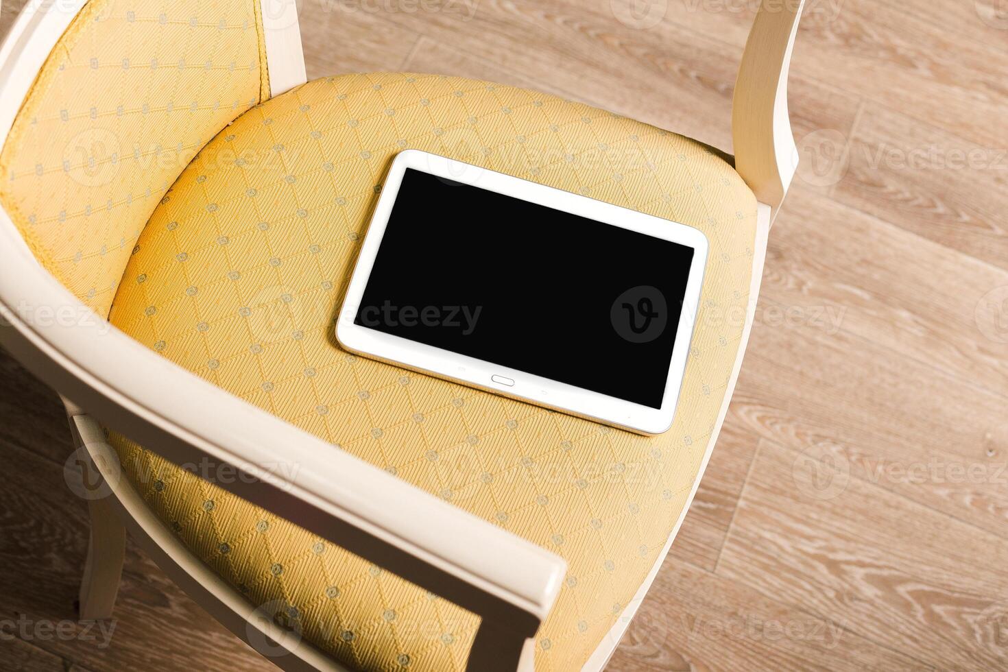 Tablet rests on a yellow upholstered chair in a cozy indoor setting during daylight photo