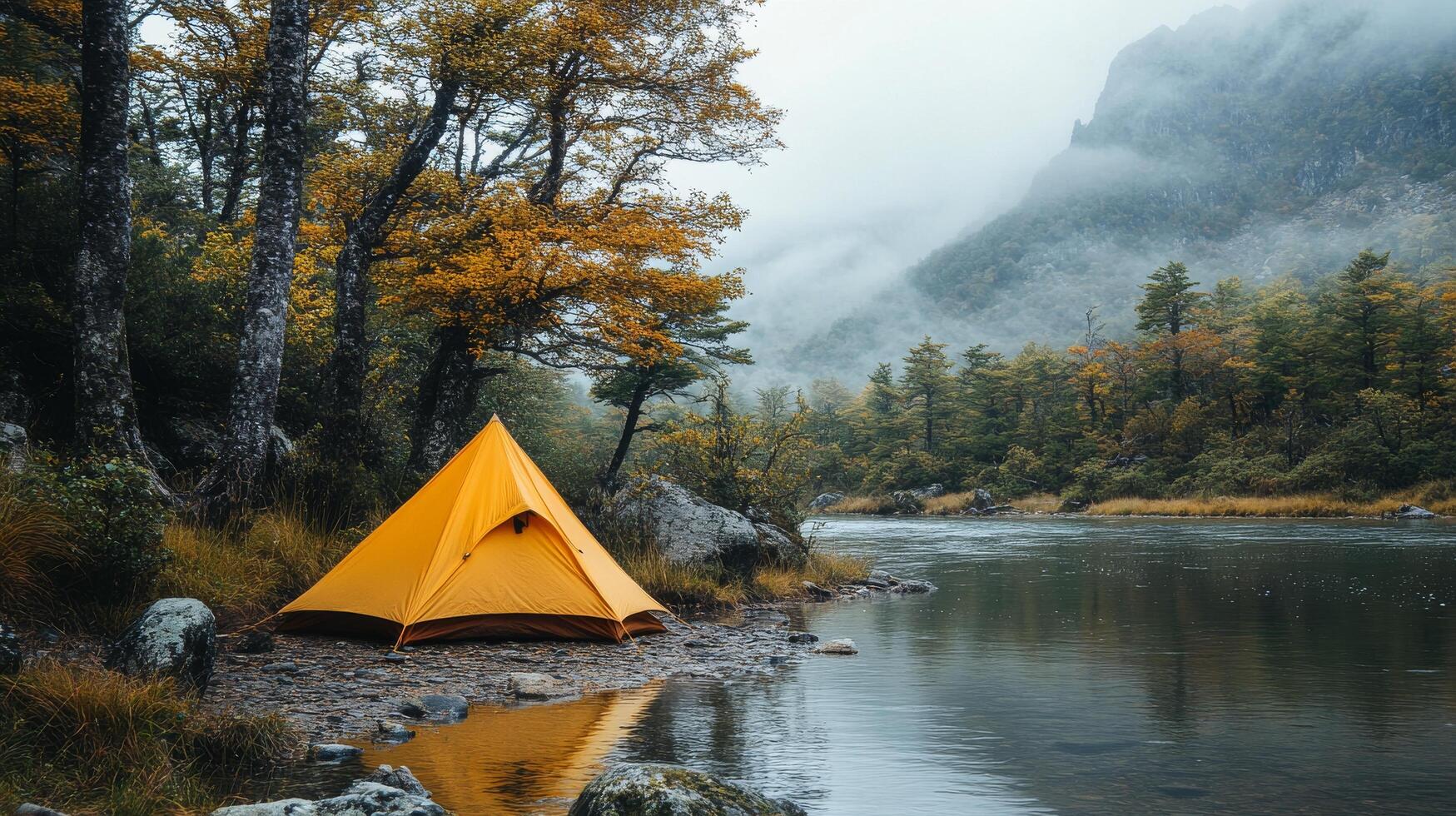 A yellow tent is set up on the shore of a river photo