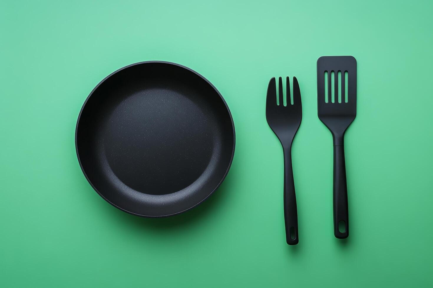 A black frying pan and fork on a green background photo