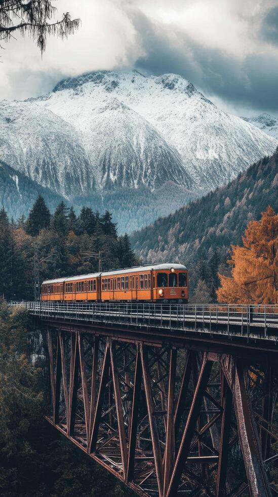An orange train traveling over a bridge in the mountains photo