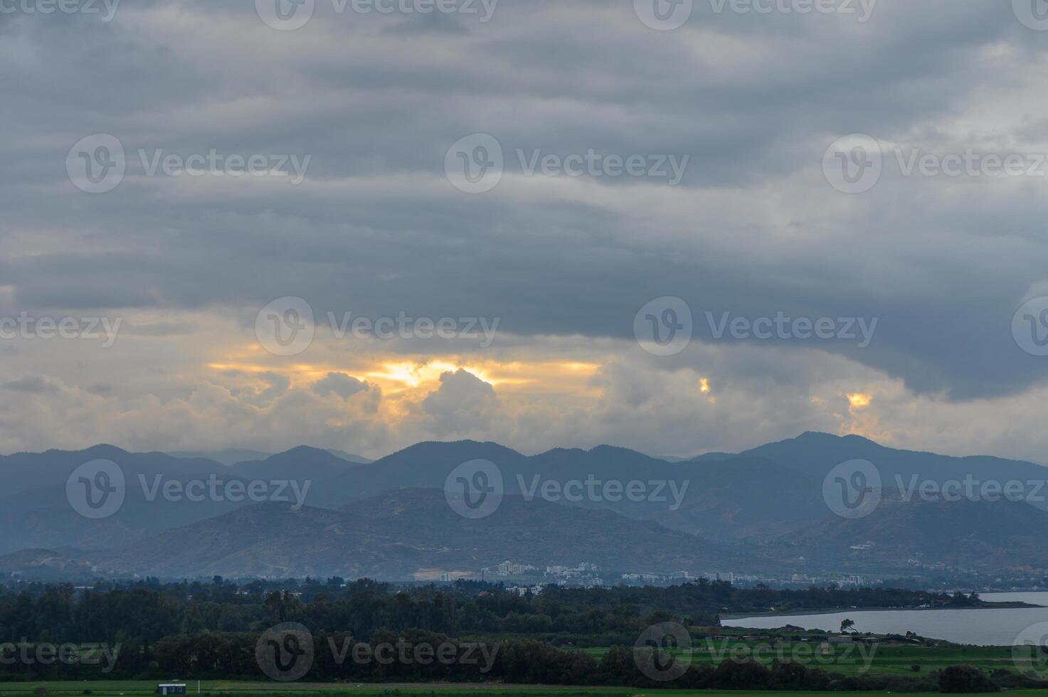 Sunlight breaks through clouds over distant mountains at dusk photo