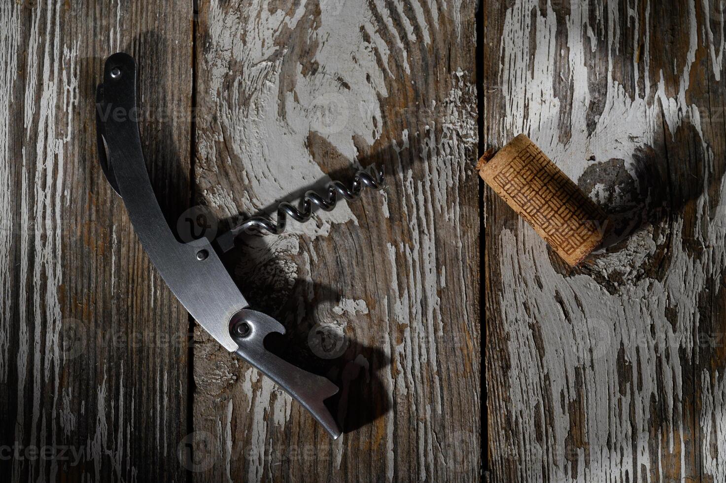 Corkscrew and cork resting on a weathered wooden surface in soft afternoon light photo