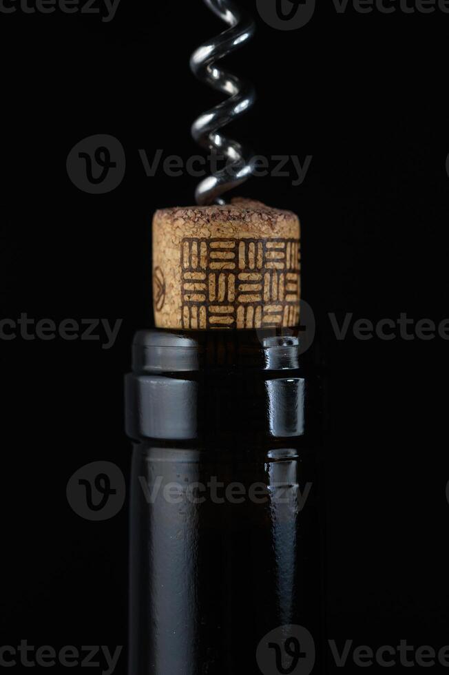 Corkscrew twisting in a bottle of dark liquid against a black background photo