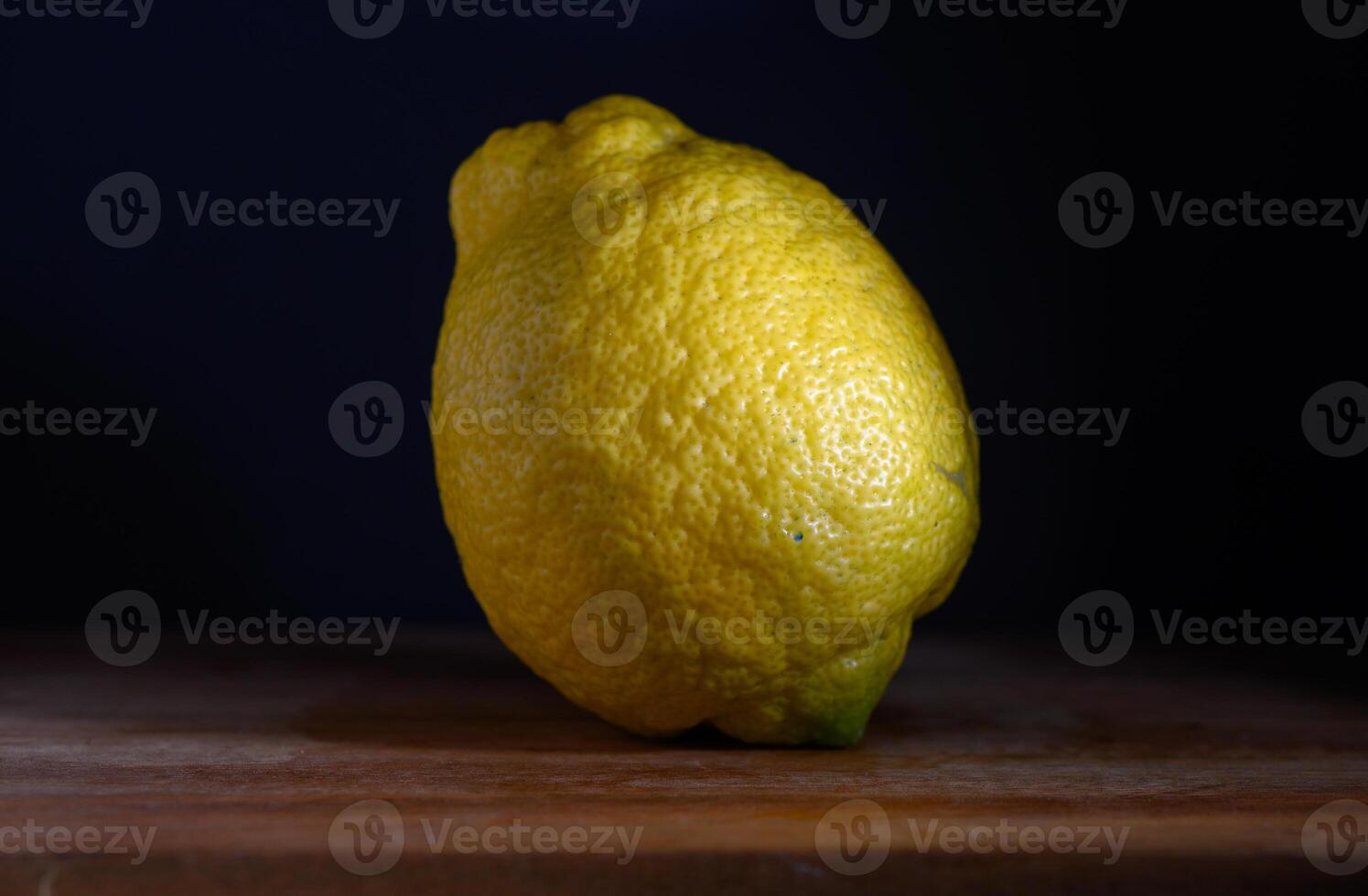 Bright lemon resting on a wooden surface against a dark backdrop under soft light photo