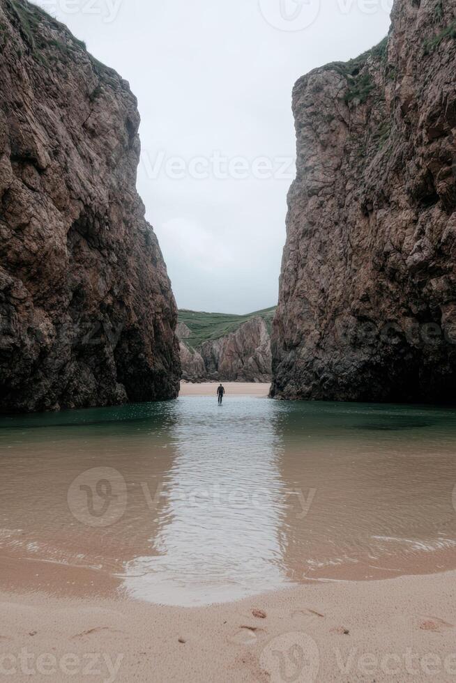 Person walking through a narrow opening between two rocky cliffs on a beach photo
