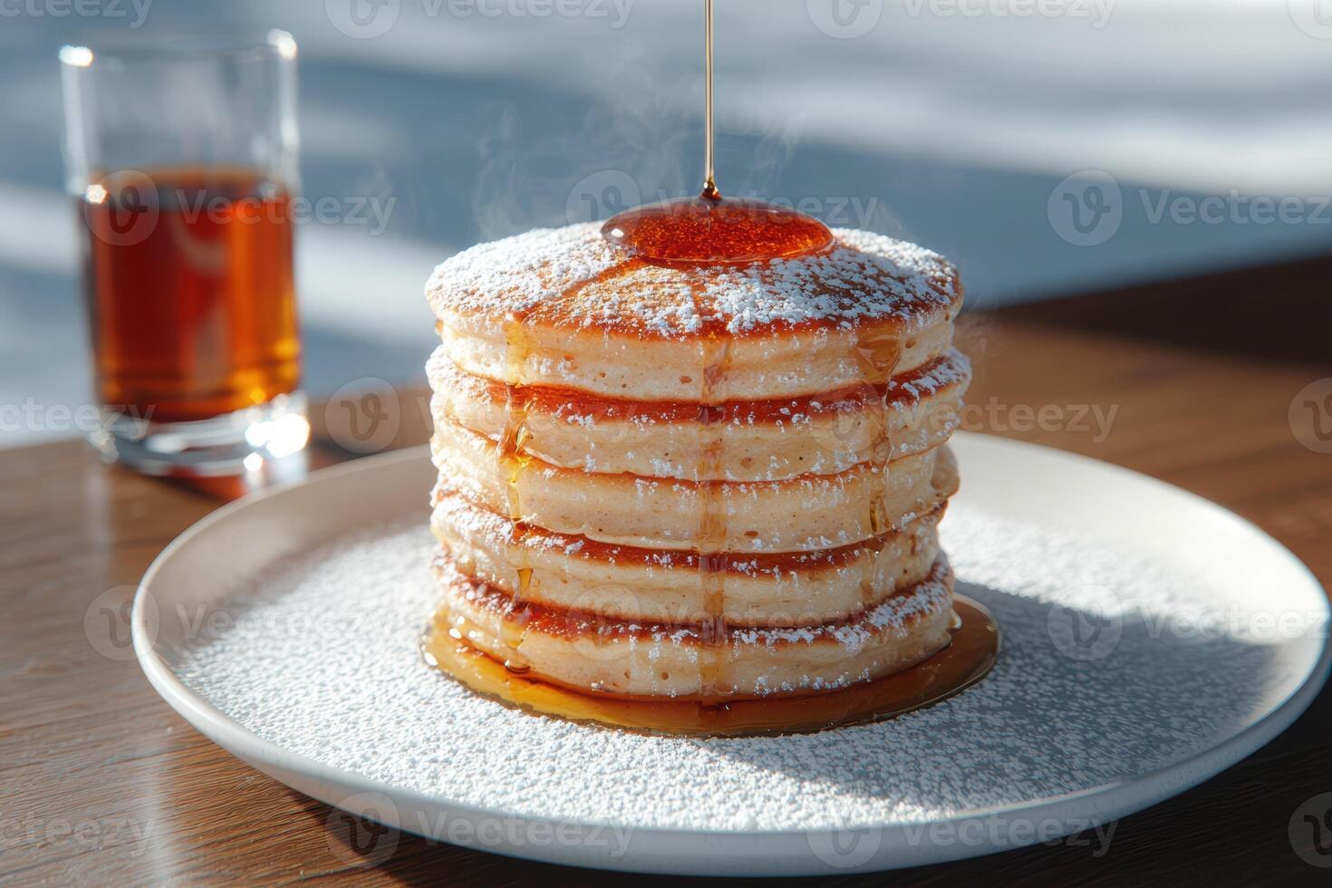 Stack of pancakes with powdered sugar and maple syrup being poured on top photo