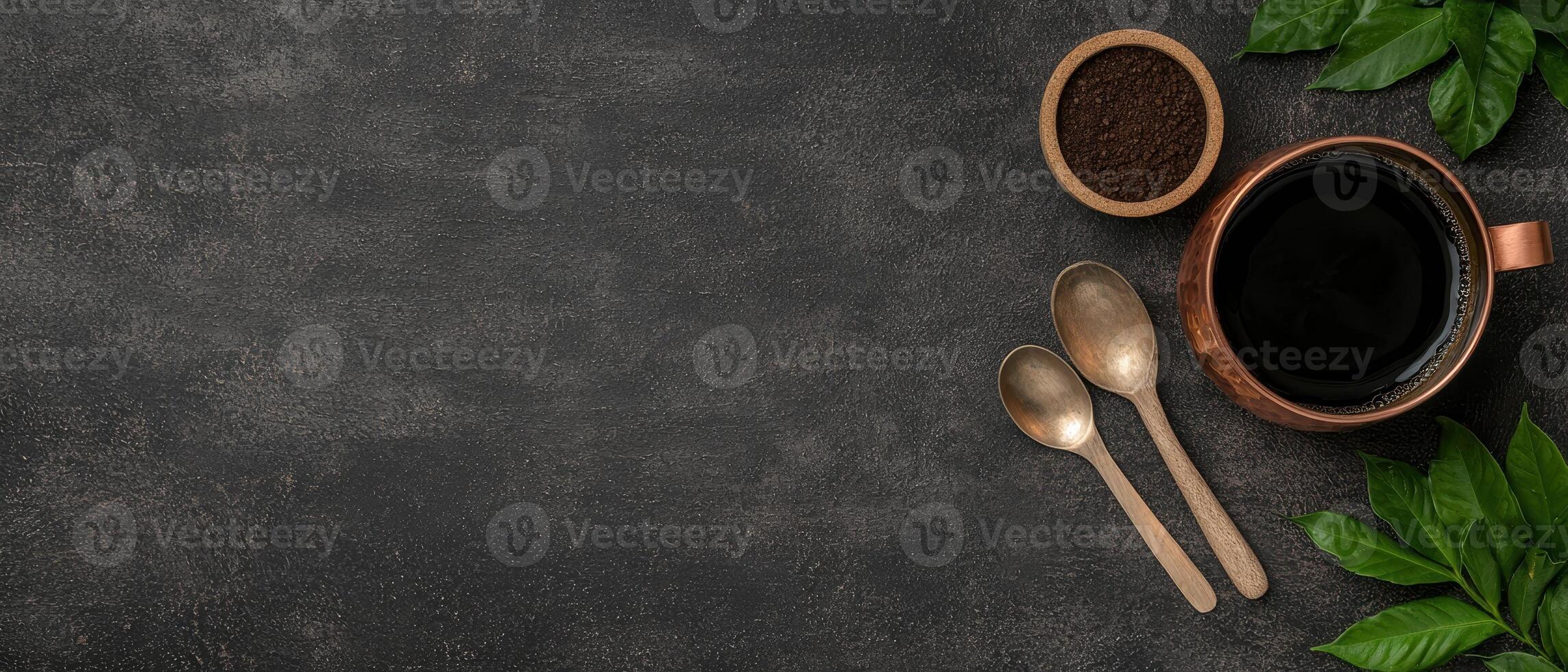 Overhead shot of coffee cup, coffee grounds, spoons, and leaves on a dark surface photo