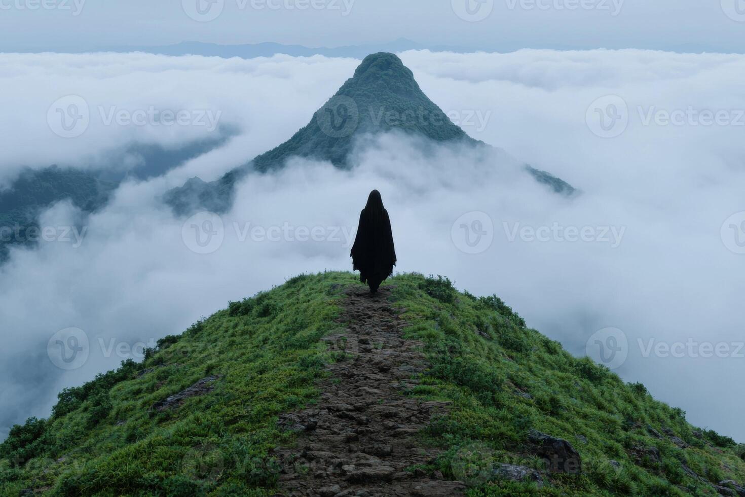 A lone figure in a cloak walks toward a mountain shrouded in mist photo