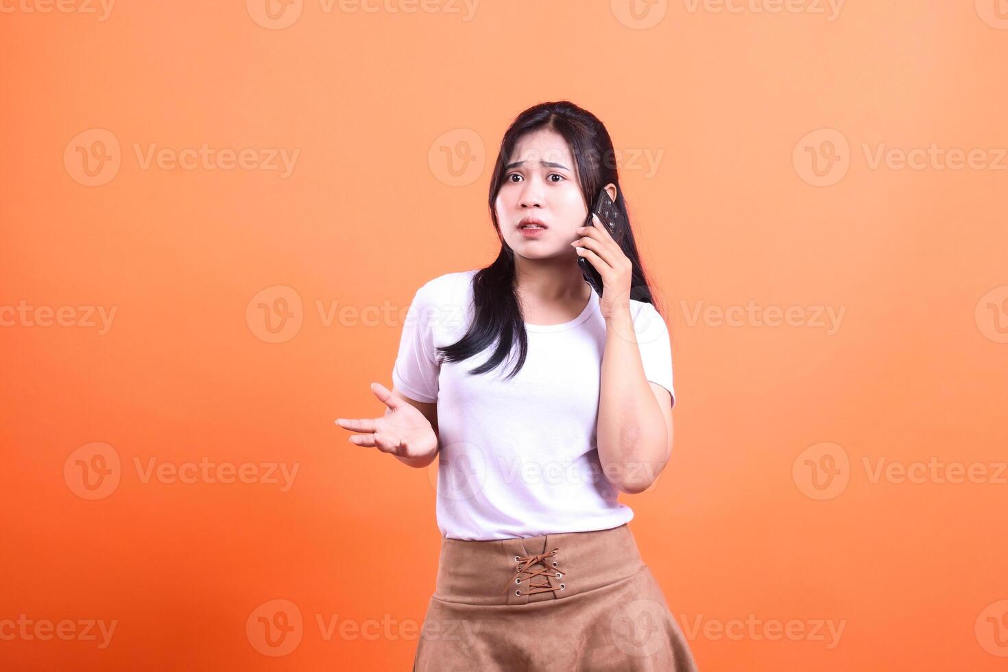 Woman in white t-shirt and brown skirt with a phone on orange background photo