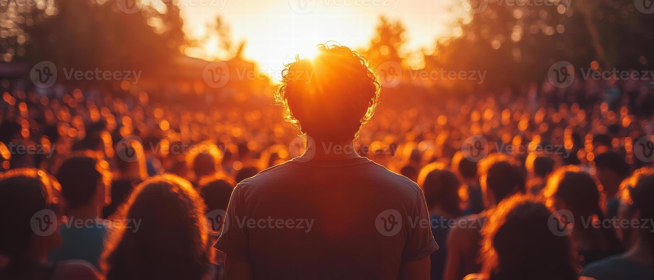 person stands in crowd during sunset, surrounded by sea of people. warm light creates vibrant atmosphere, evoking feelings of connection and community photo