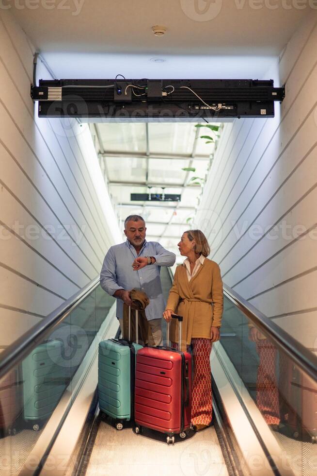 vertical Senior couple checking time on moving walkway at airport photo