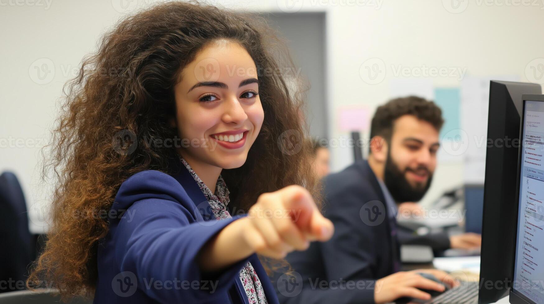 young woman with curly hair, standing in front of a computer monitor photo