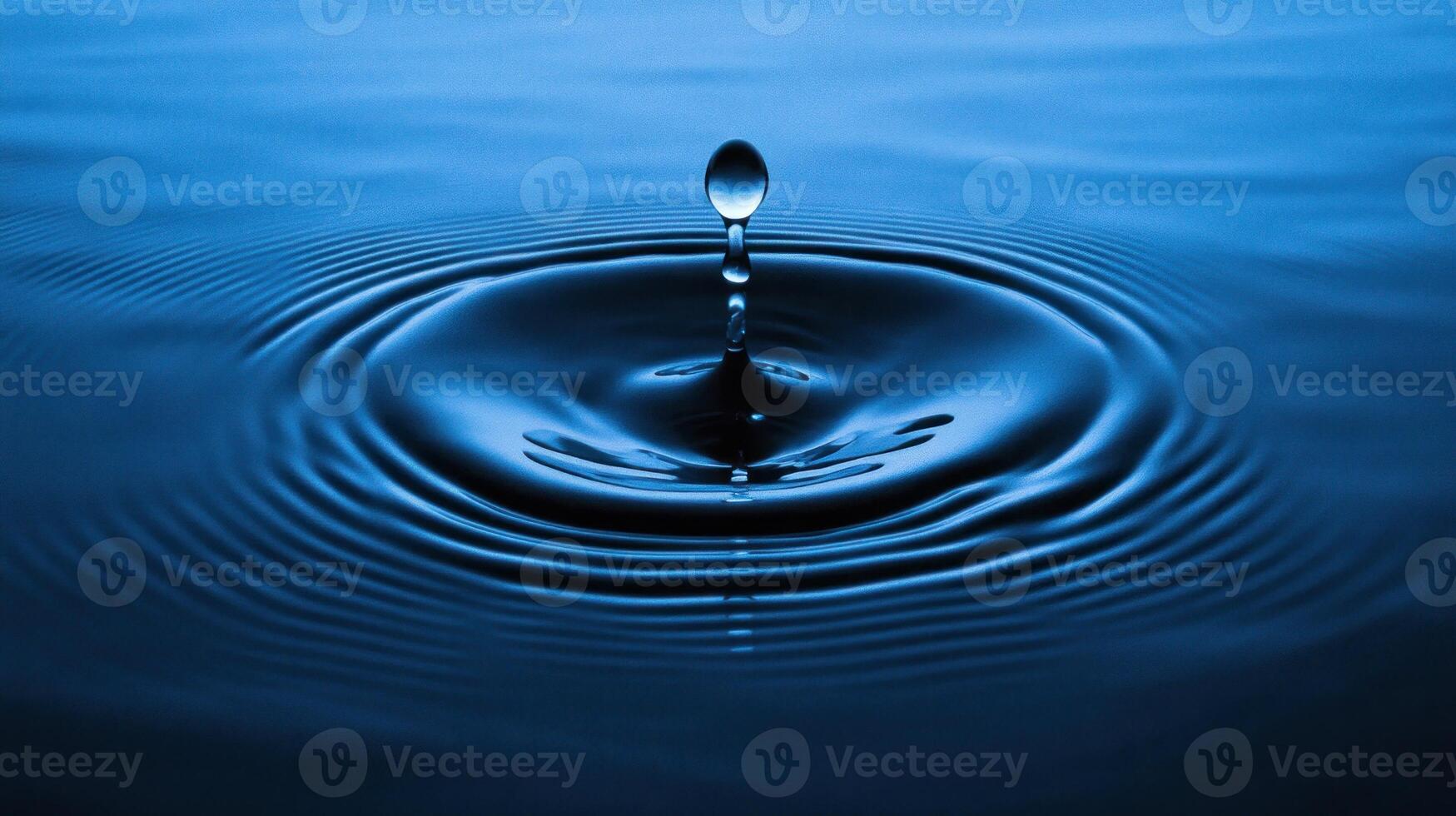 A droplet falls into still water, generating concentric circles that radiate outward in serene blue photo