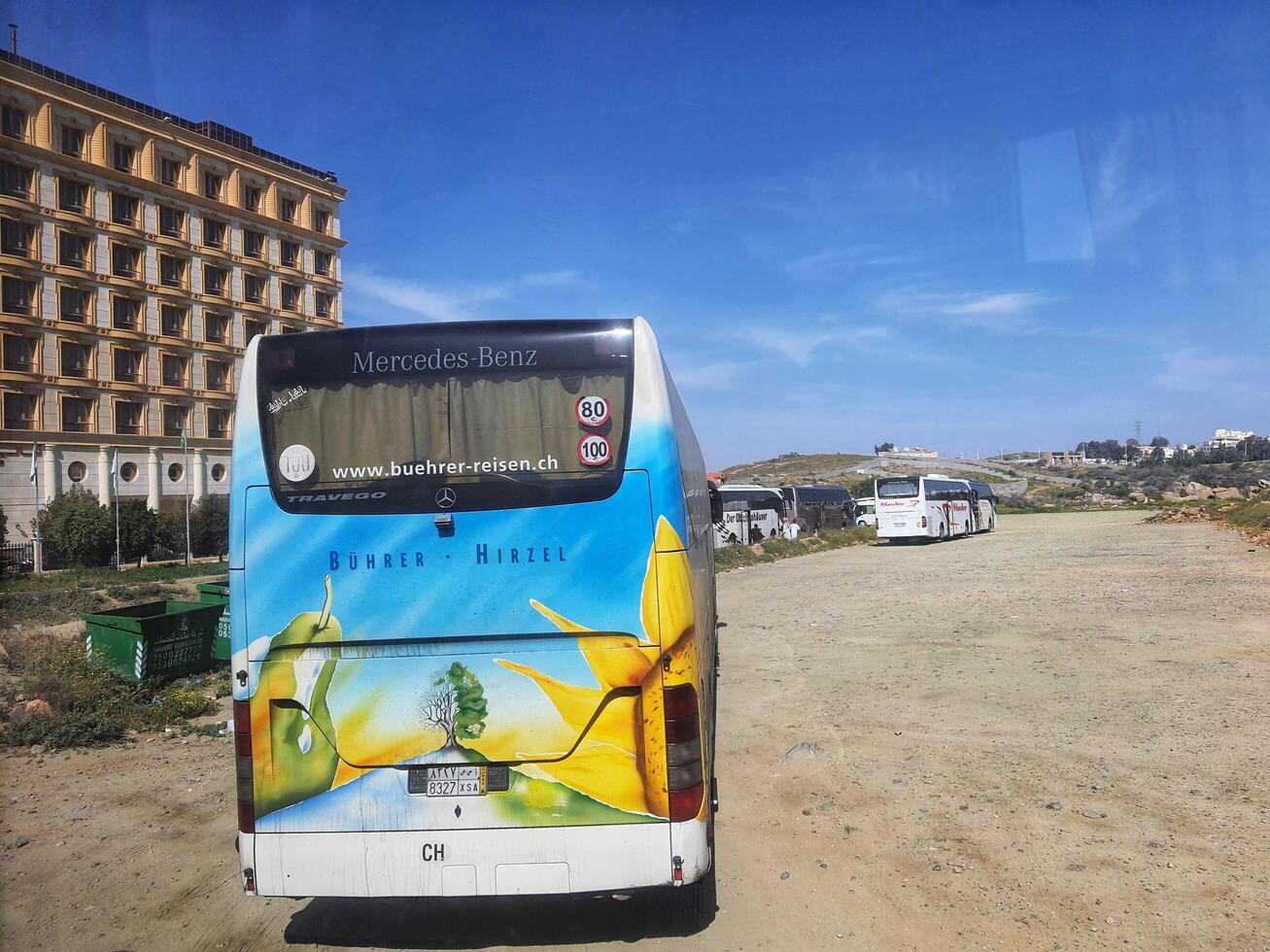 Mecca, Saudi Arabia on 24 February 2024. Colorful Bus Mercedes Benz Parked Near Hotel Sunny Day photo