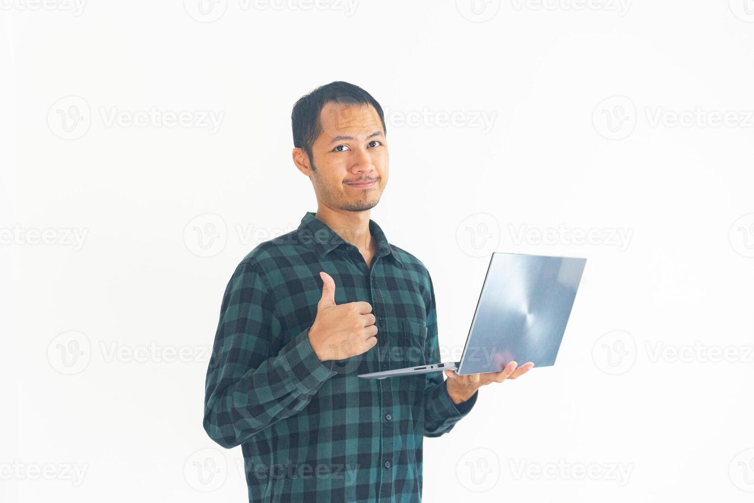 Young bearded man give thumbs up while holding laptop on isolated background photo