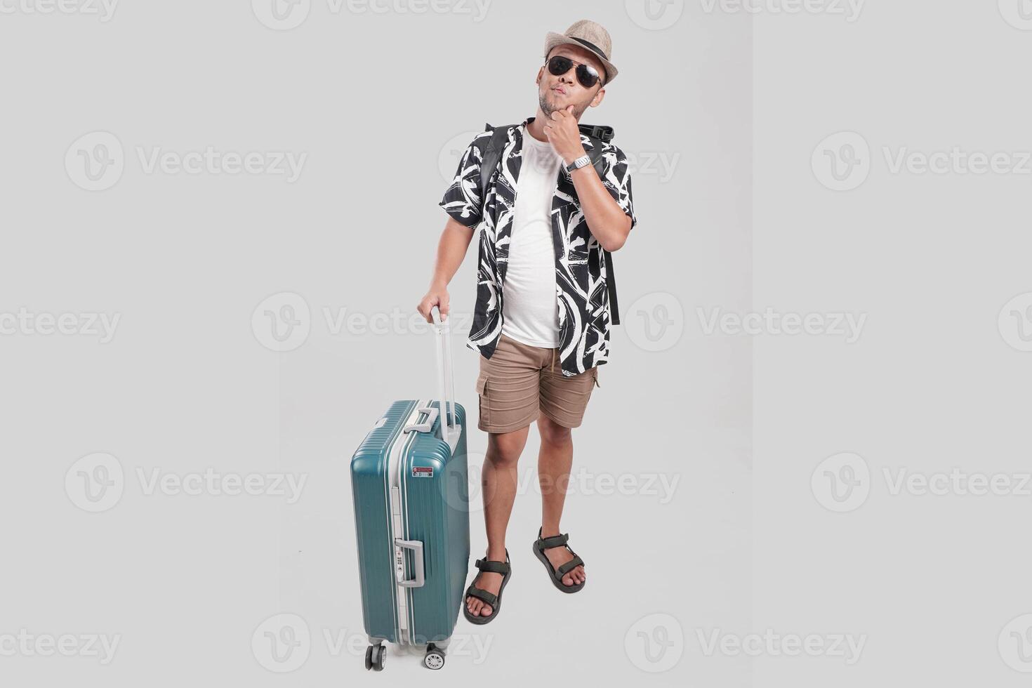 Thoughtful young Asian man traveler with suitcase holding his chin while thinking of an idea. photo