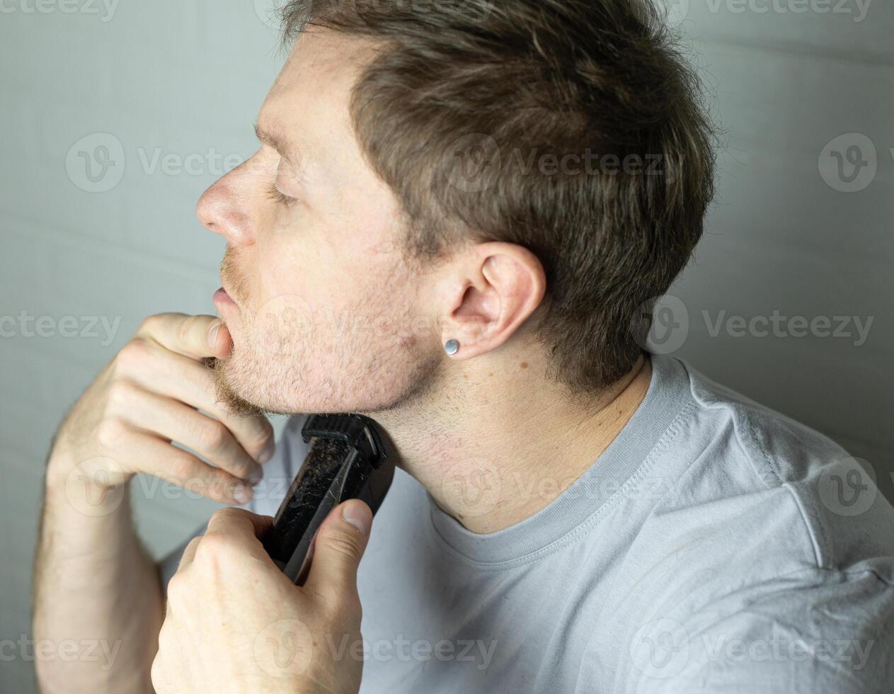 a man trims his beard with a trimmer. Close up. An electric razor trimming a beard. Beard care at home. photo
