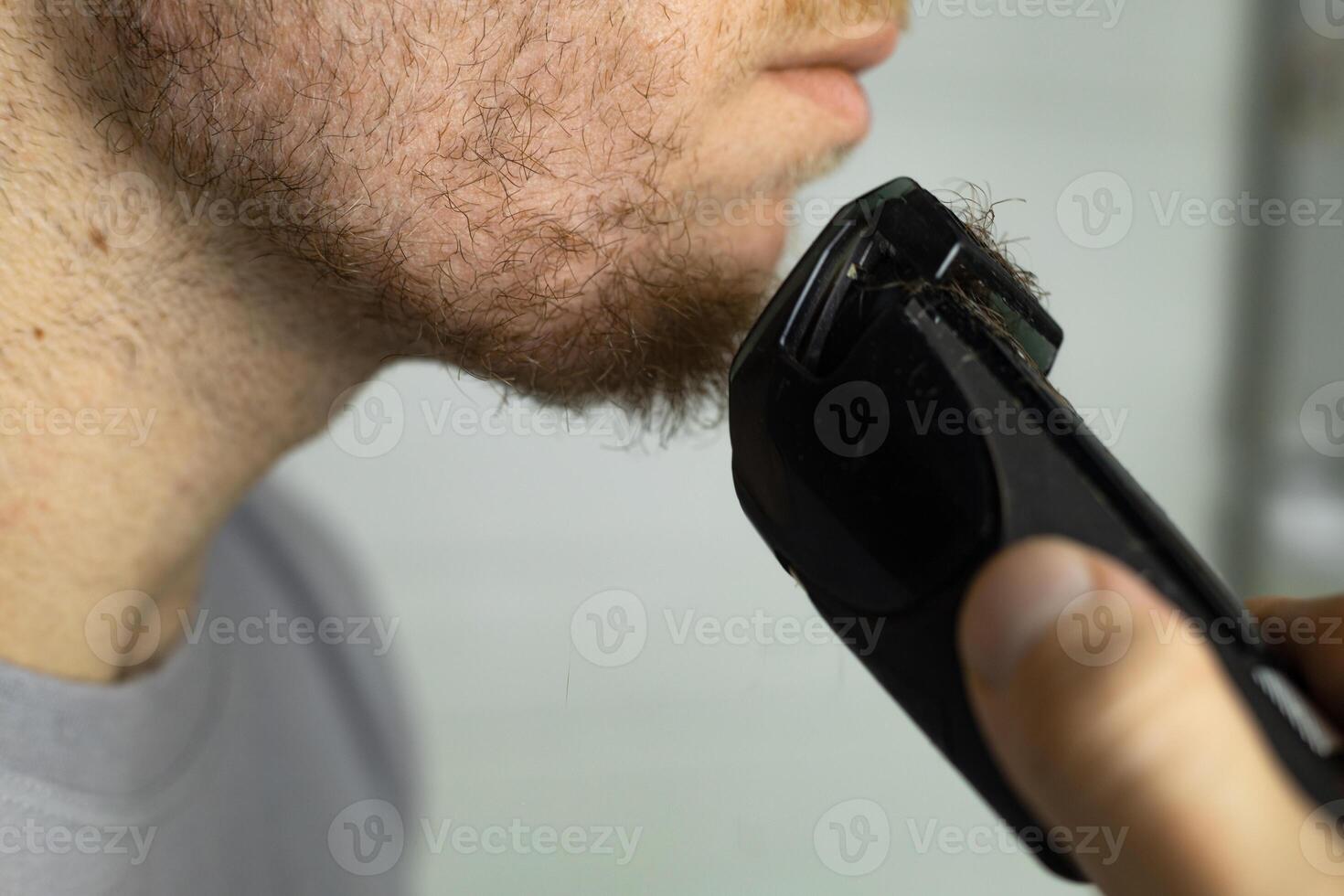 An electric razor trimming a beard. man trims his beard with a trimmer. photo