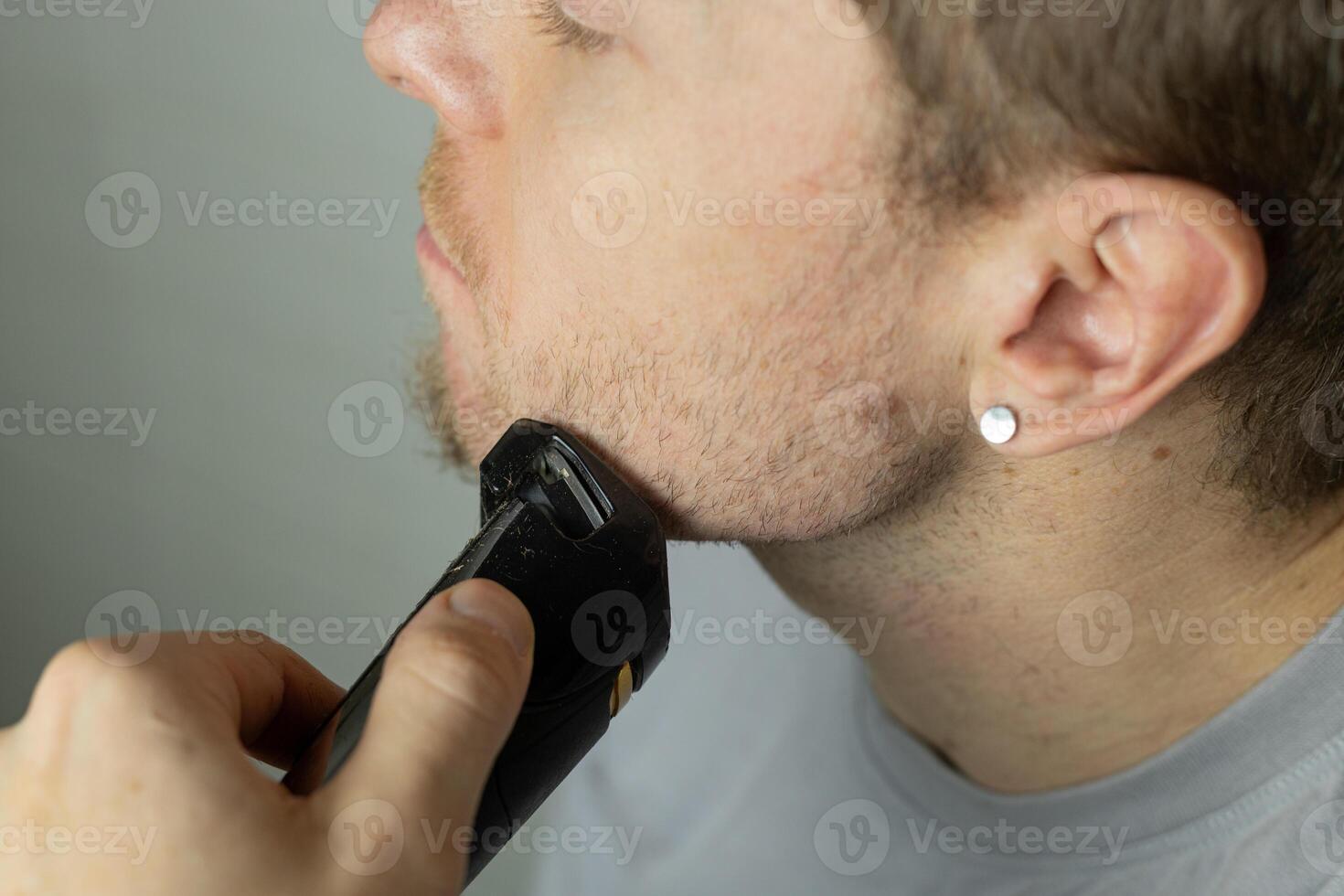 man trims his beard with a trimmer. An electric razor trimming a beard. Beard care at home. photo