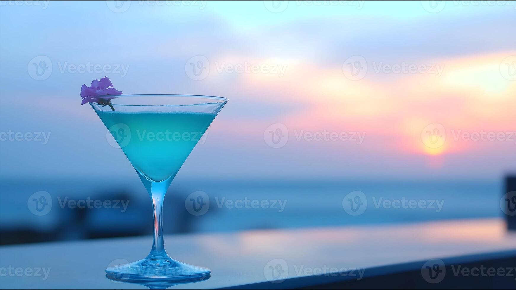 A blue martini glass with a flower on top is sitting on a table by the ocean photo