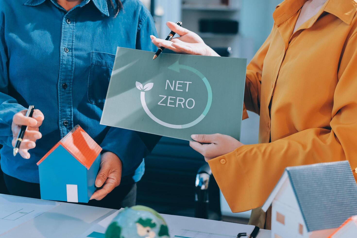 Two people holding a net zero sign and a house photo