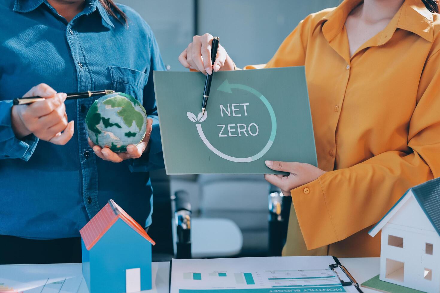 Two people holding a net zero sign and a house photo