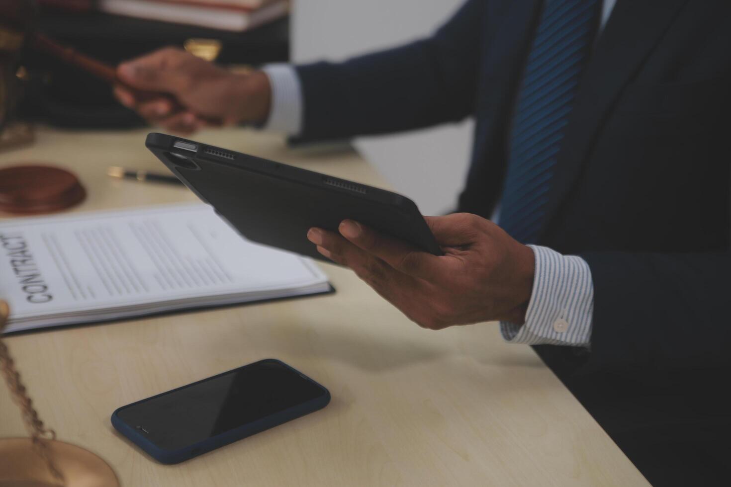 A man in a suit holding a tablet and a smartphone in front of a judge's gavel photo