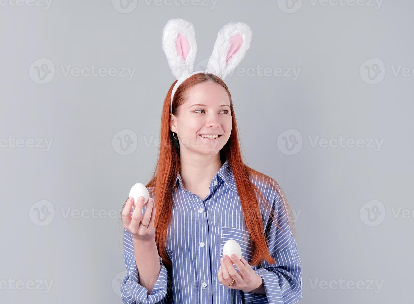 woman wearing rabbit ears holding eggs isolated over light gray color background photo