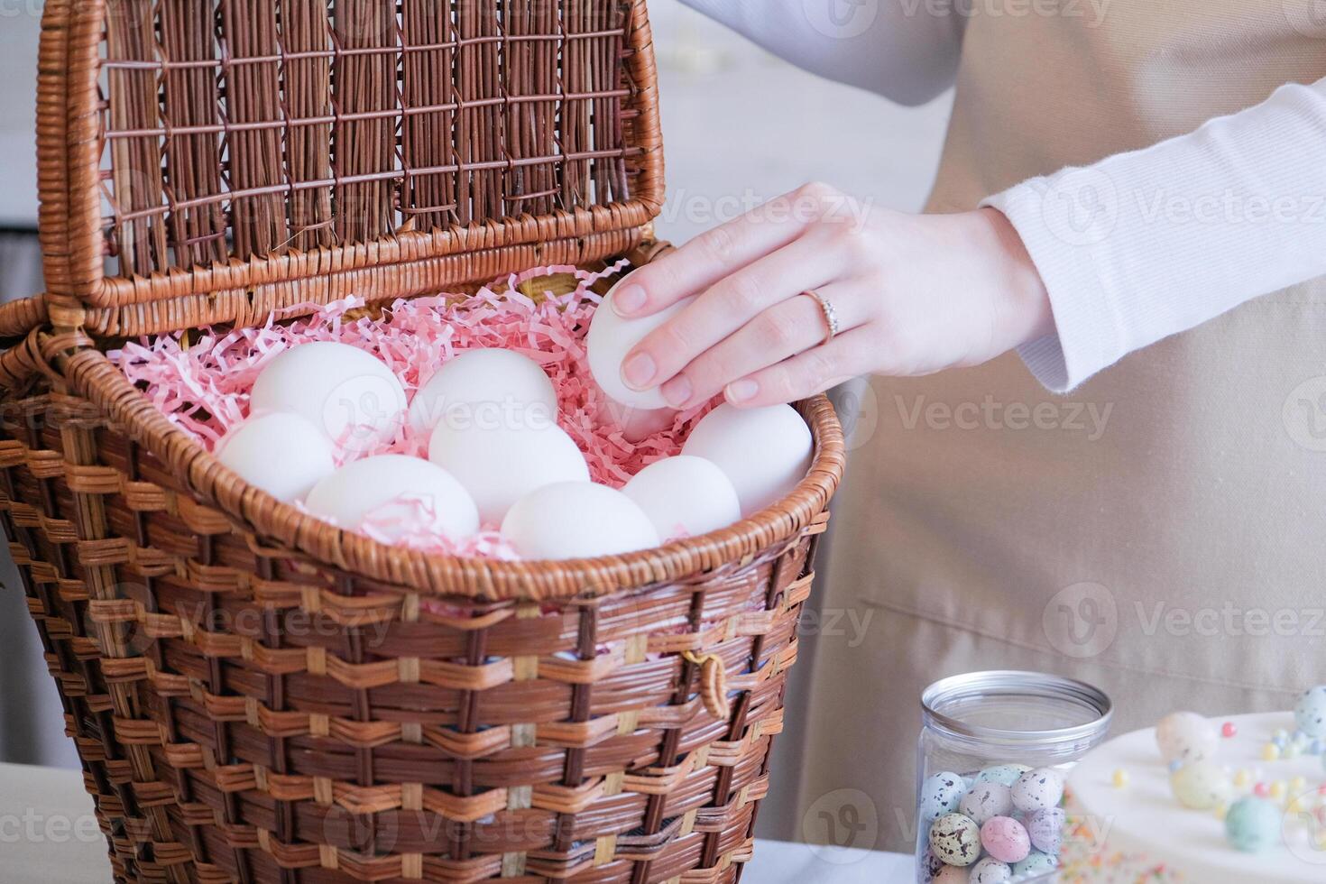 unrecognizable woman in apron putting the white eggs into the basket, getting ready for Easter photo