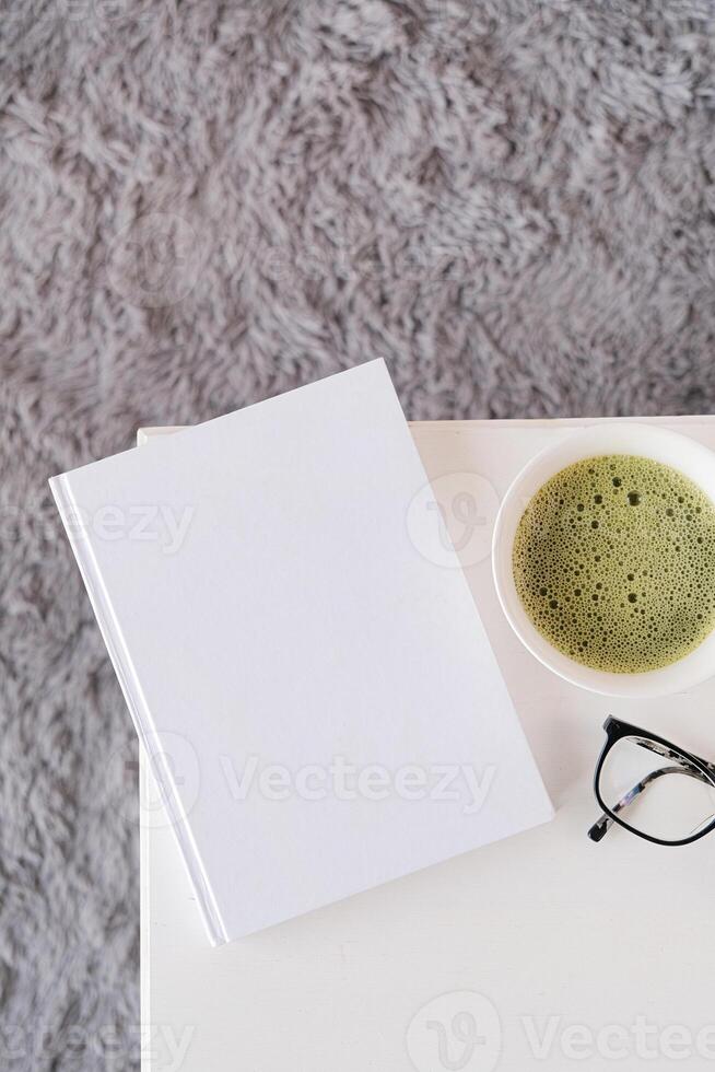 blank white book template on white coffee table with green matcha tea near window photo