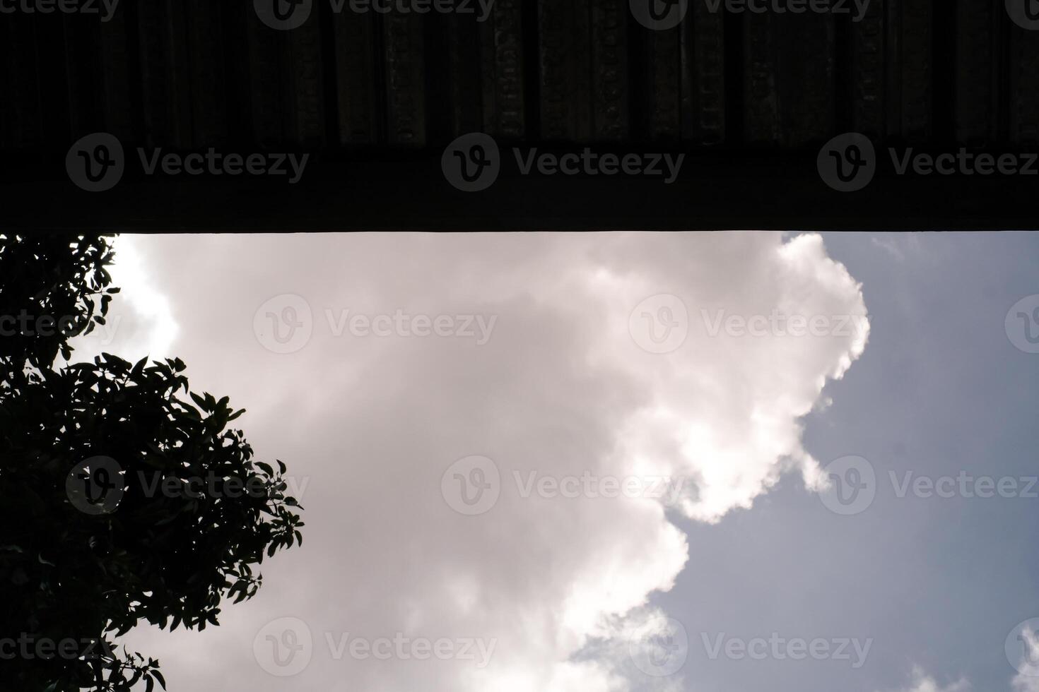 The blue sky is partially covered by the roof. One side shows a cloudy sky and the other side is covered by a roof. Low angle shot. Wallpapers Backgrounds. Negative Space. photo