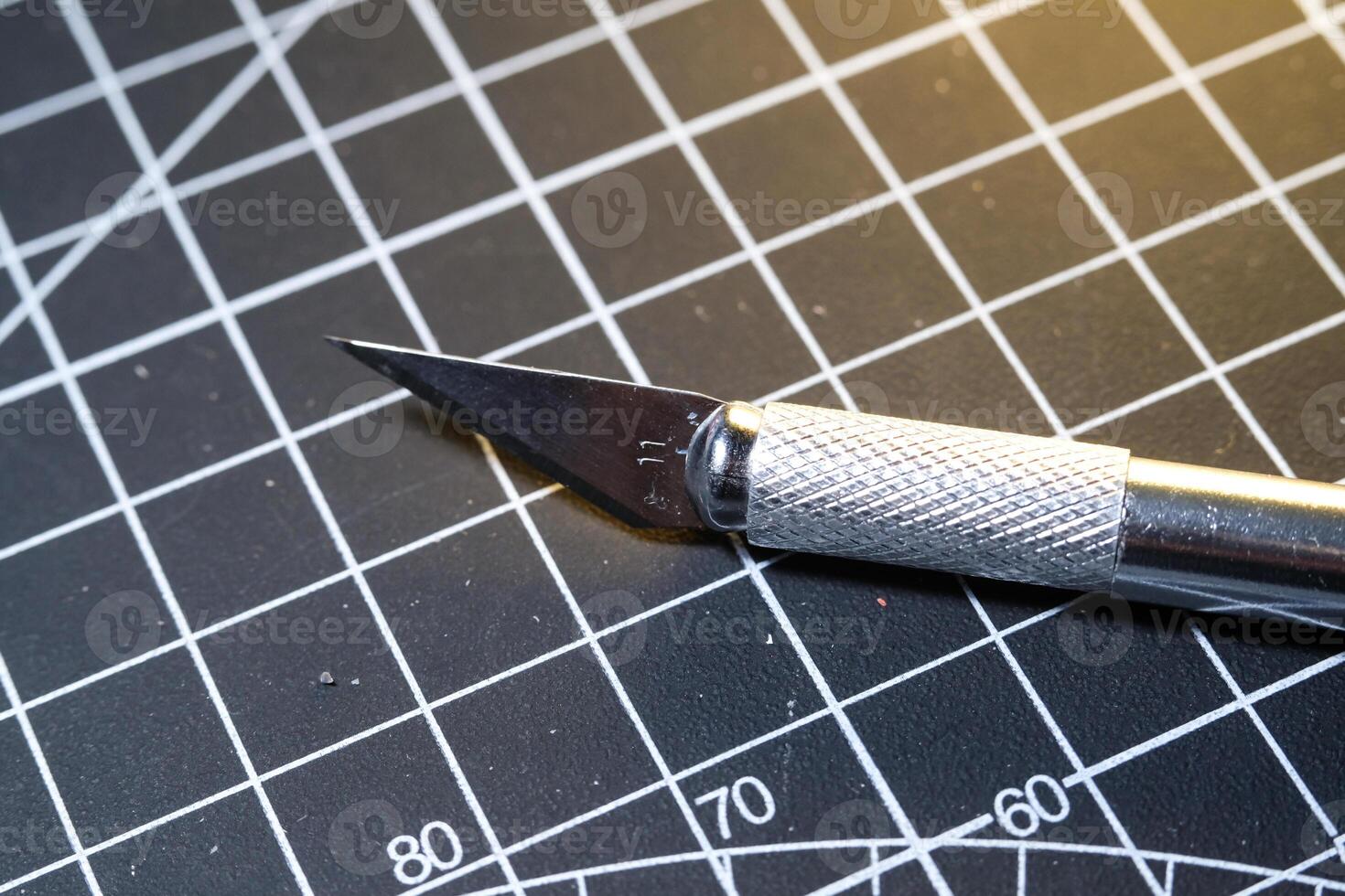 Cutting blade on black striped rubber mat. Sharp cutting blade used to cut plastic parts. Metal tools and equipment. Tools for hobbyist robot model kit assembly. photo